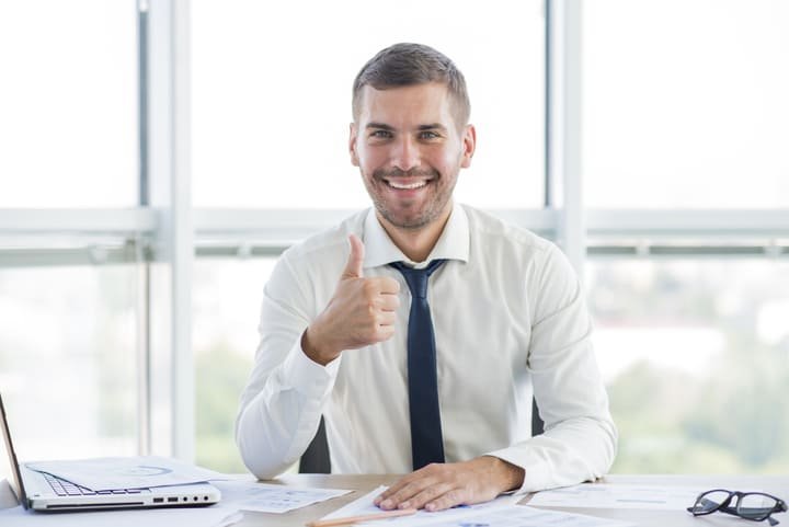 Homem fazendo sinal de positivo em mesa de escritório simulando registro de marcas aprovado