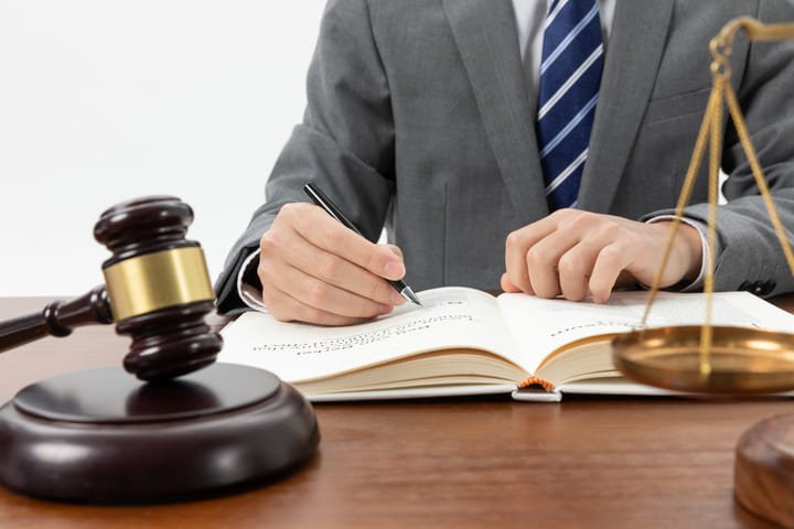 Homem escrevendo em livro com símbolos do direito sob a mesa representando lei de propriedade industrial