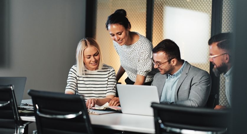 Equipe de 5 empreendedores, dois homens e duas mulheres em um escritório lendo sobre Inovação no empreendedorismo em um computador