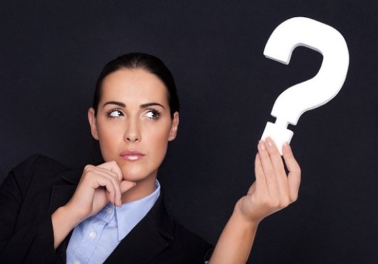 Beautiful businesswoman with a thoughtful expression holding a white question mark in her hand against a black studio background